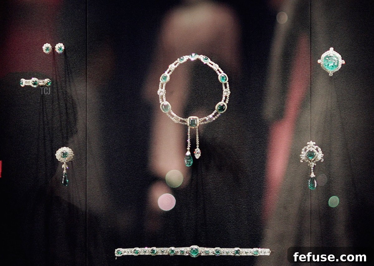 Queen Elizabeth II's historic dresses reflected in a display case featuring the Vladimir Tiara and the Delhi Durbar necklace at Buckingham Palace, showcasing pieces with Cambridge Emeralds.