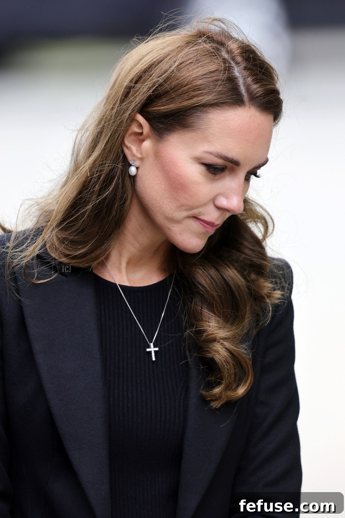 Catherine, Princess of Wales, in solemn black, views floral tributes at Sandringham, wearing pearl drop earrings and a delicate diamond cross pendant.