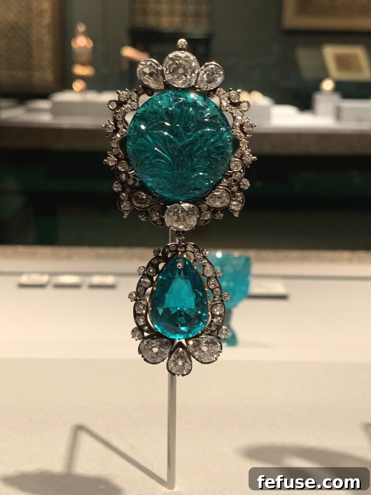 Detailed view of a beautifully carved emerald brooch with diamond accents and a striking faceted emerald pendant