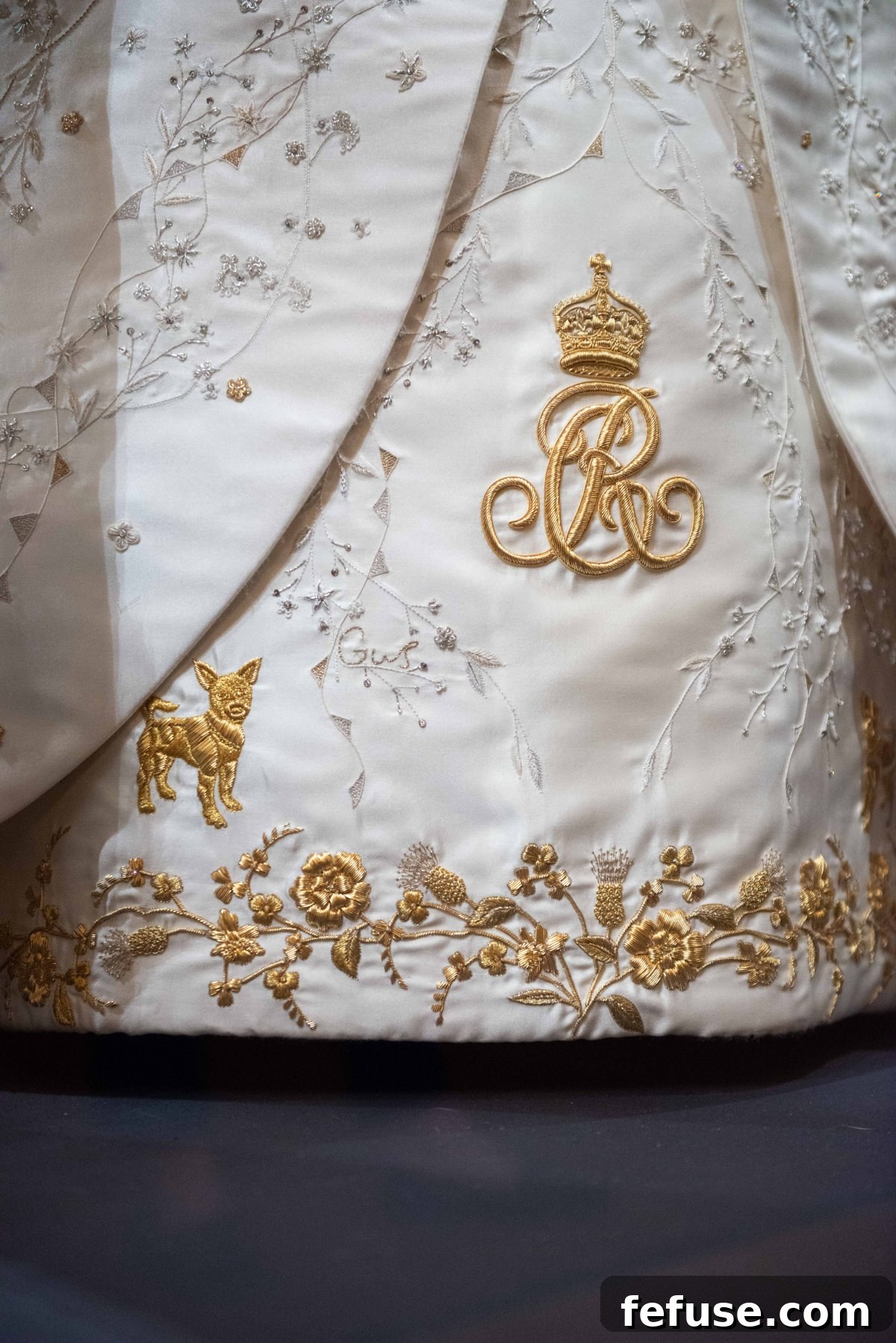 Detailed embroidery on Queen Camilla's Coronation Dress, showcasing wildflowers, national emblems, and personal touches like her royal cypher and grandchildren's names, at the Buckingham Palace exhibition, July 2023. (Royal Collection Trust)