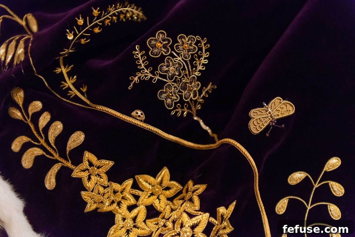 Close-up of the exquisite embroidery on Queen Camilla's Robe of Estate, showing symbolic flowers like Scabiosa, Lily of the Valley, and Delphinium, exhibited at Buckingham Palace, July 2023. (Royal Collection Trust)